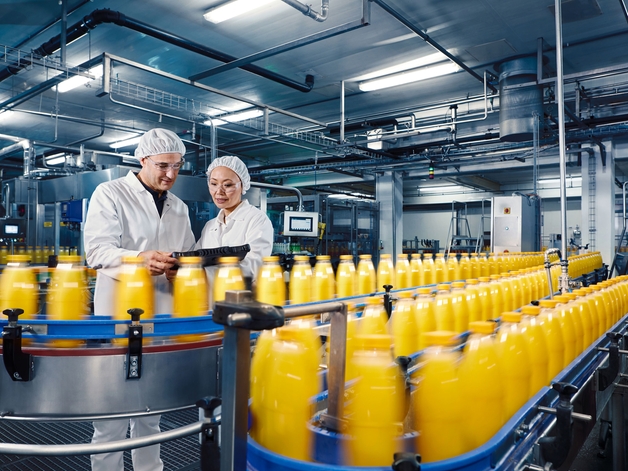 Dos ingenieros en una fábrica de bebidas supervisan el proceso de llenado de zumo de naranja.